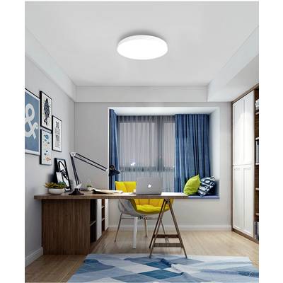 A modern home office with a wooden desk, yellow chair, laptop and desk lamp. A large window with blue curtains in the background.