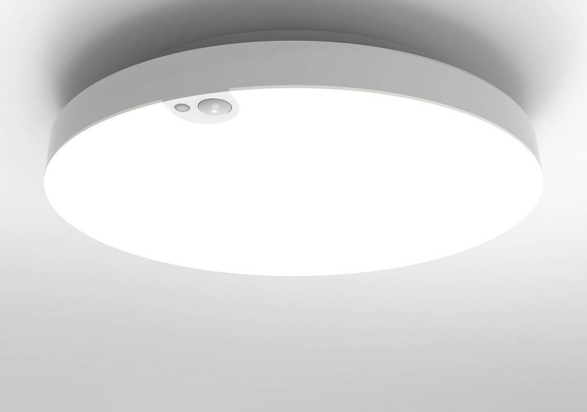 Round, white ceiling light with built-in motion sensor shines brightly on a grey ceiling.