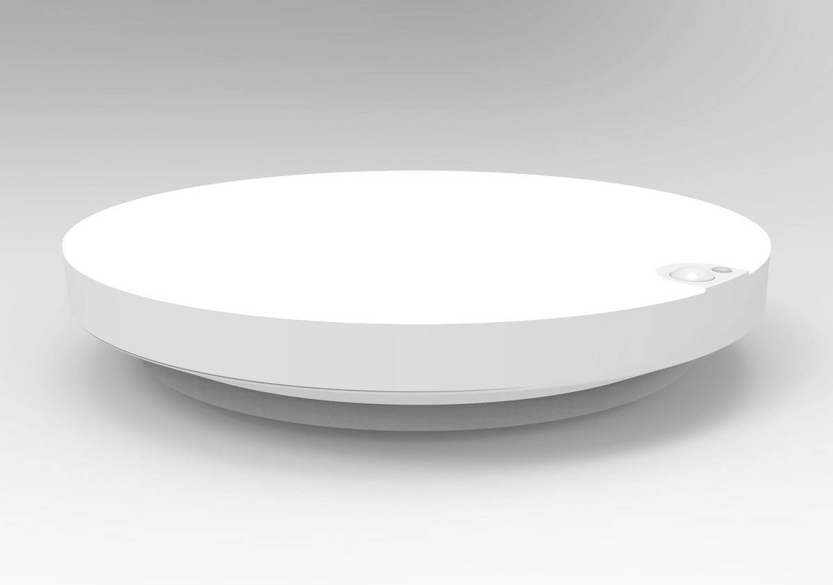 A round, white smoke detector with a side button is lying on a smooth surface.
