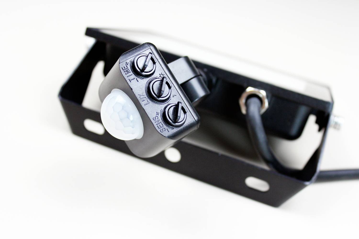 A black motion sensor with three adjustment dials for 'TIME', 'LUX' and 'SENS', mounted on a bracket with a cable connection.