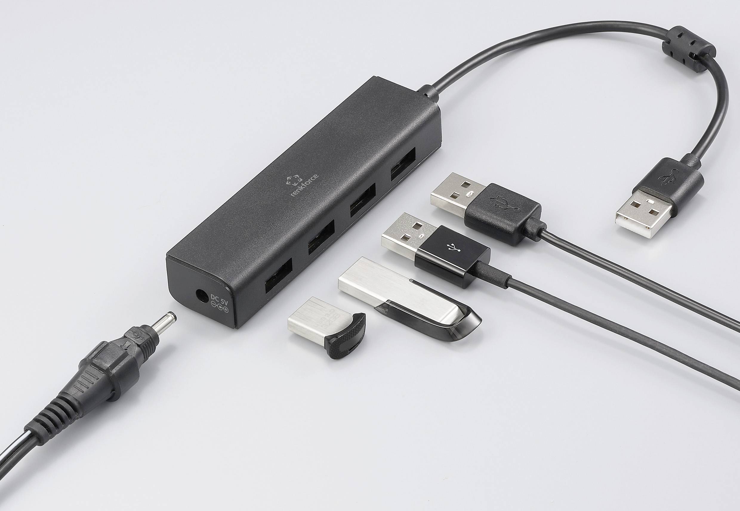 A USB hub with four ports, connected with USB cables and plugs. Beside it lies another cable with a round plug.