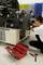 A technician is repairing an industrial machine. A toolbox and tools are lying on the floor. Coloured storage boxes are in the background.