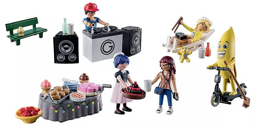 Playmobil scene with a DJ, waitress, two women, a sunbather, and a banana figure on a scooter. In the foreground, a table with cake.