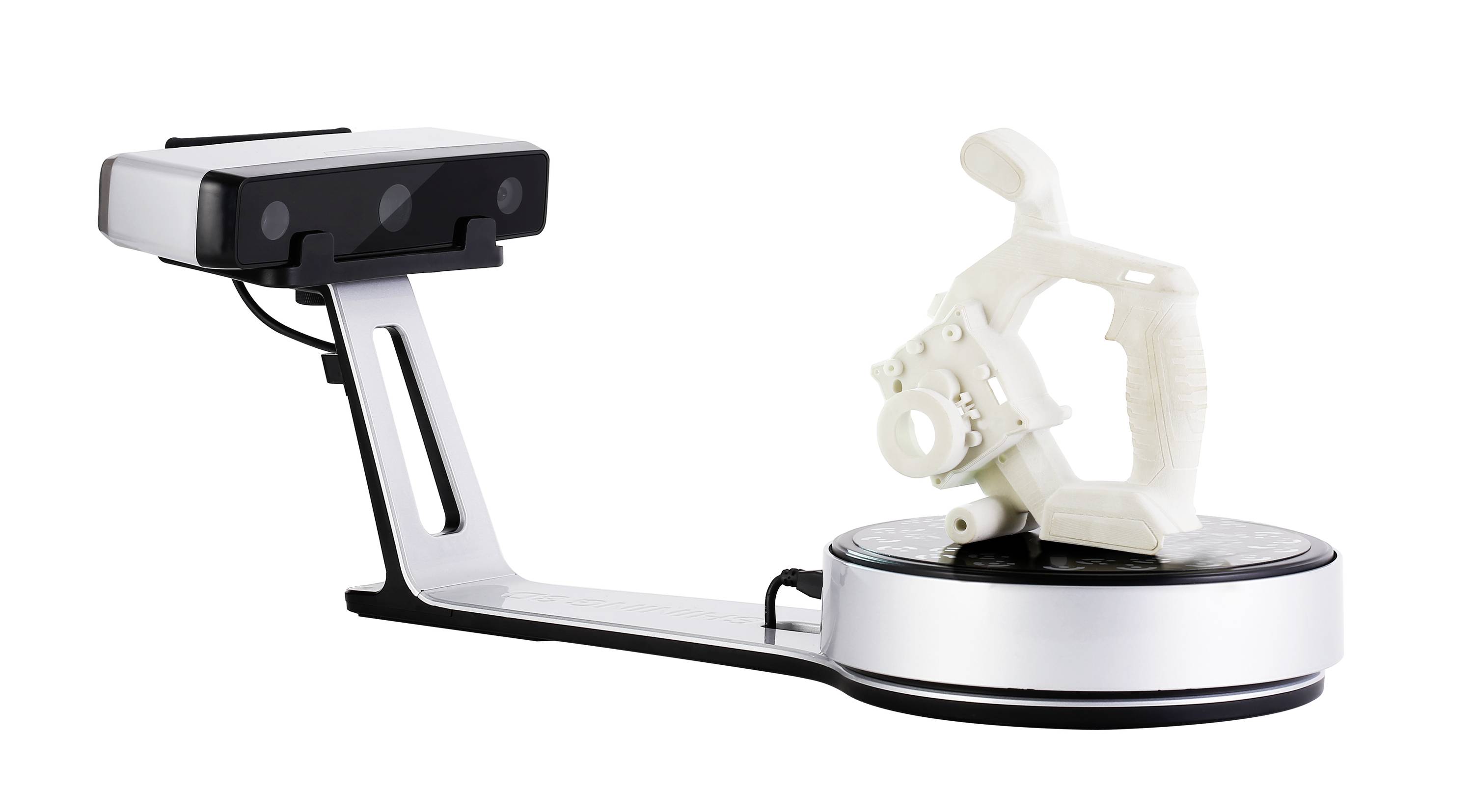 A 3D scanner captures a white, geometric object on a turntable. The scanner has a long mounting arm and a rectangular camera.