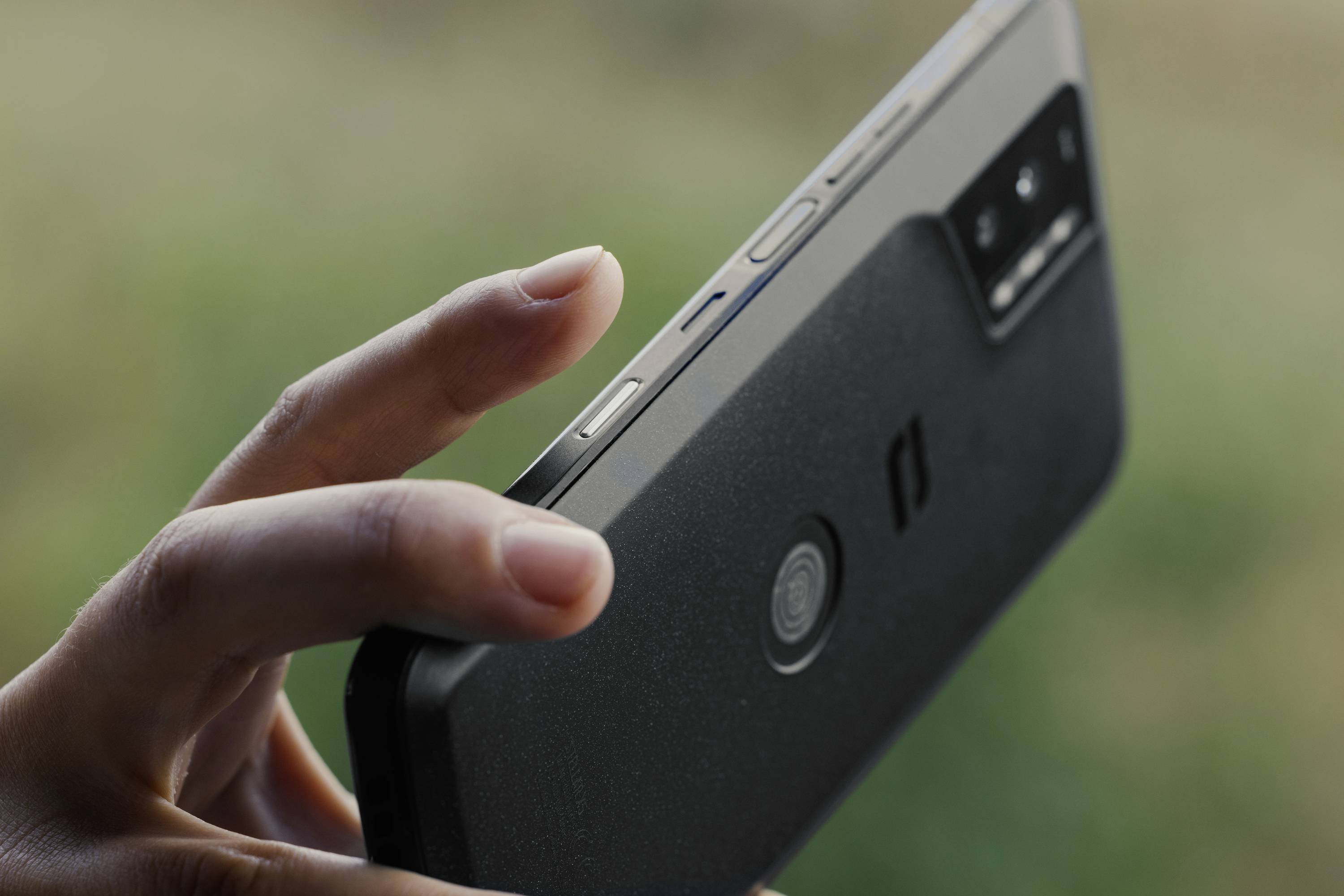 A hand is holding a smartphone nearby, with the screen not visible. The focus is on the control buttons and the camera.