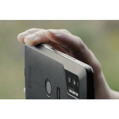 A hand holding a smartphone, viewed from the side. The camera and volume buttons are visible. Background blurred.