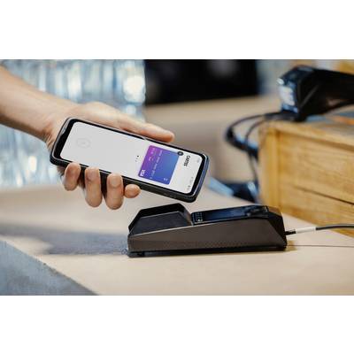 A hand is holding a smartphone with an open payment app over a card terminal used for contactless payment.