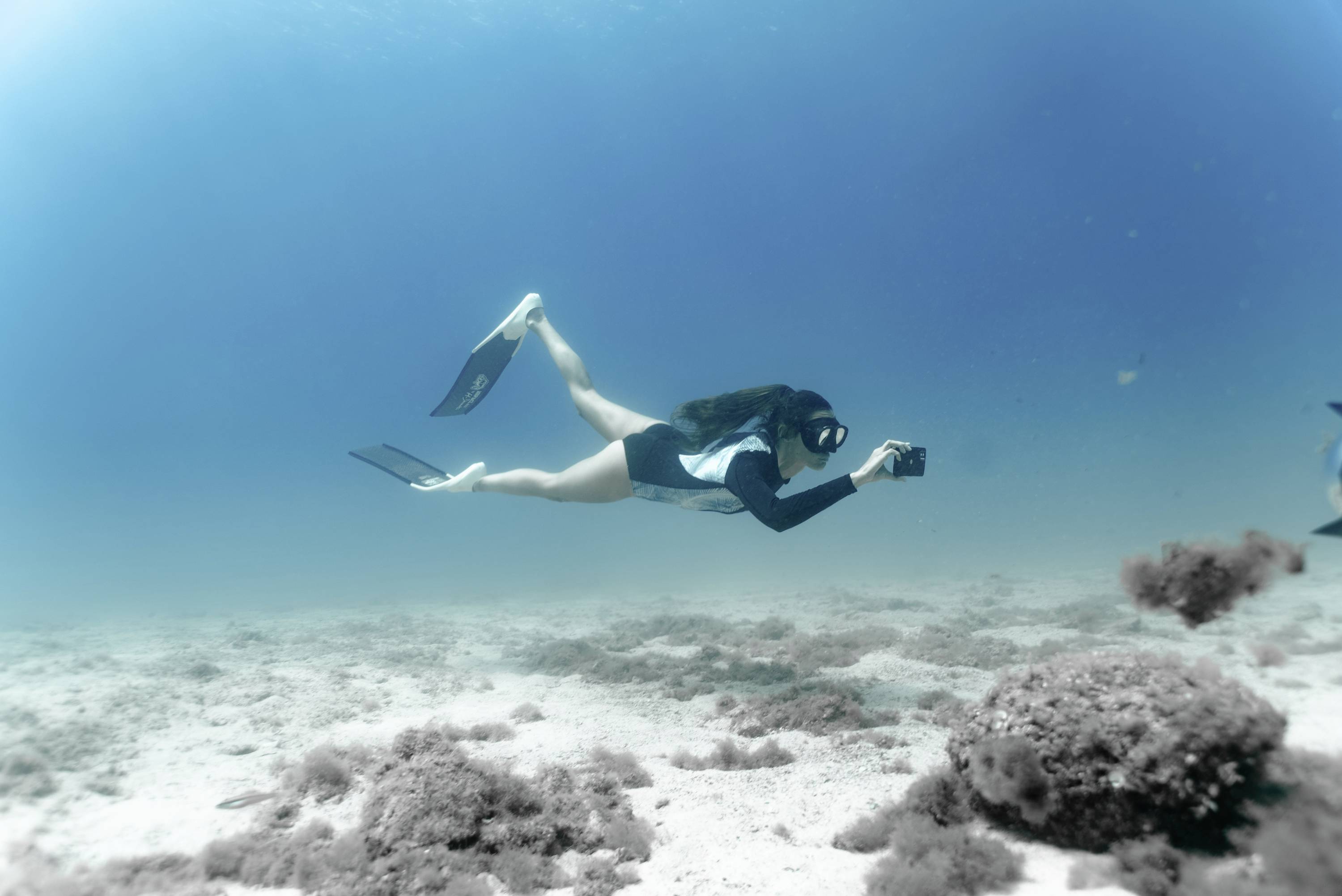 A person is snorkelling underwater and holding a camera to capture images of the marine environment.
