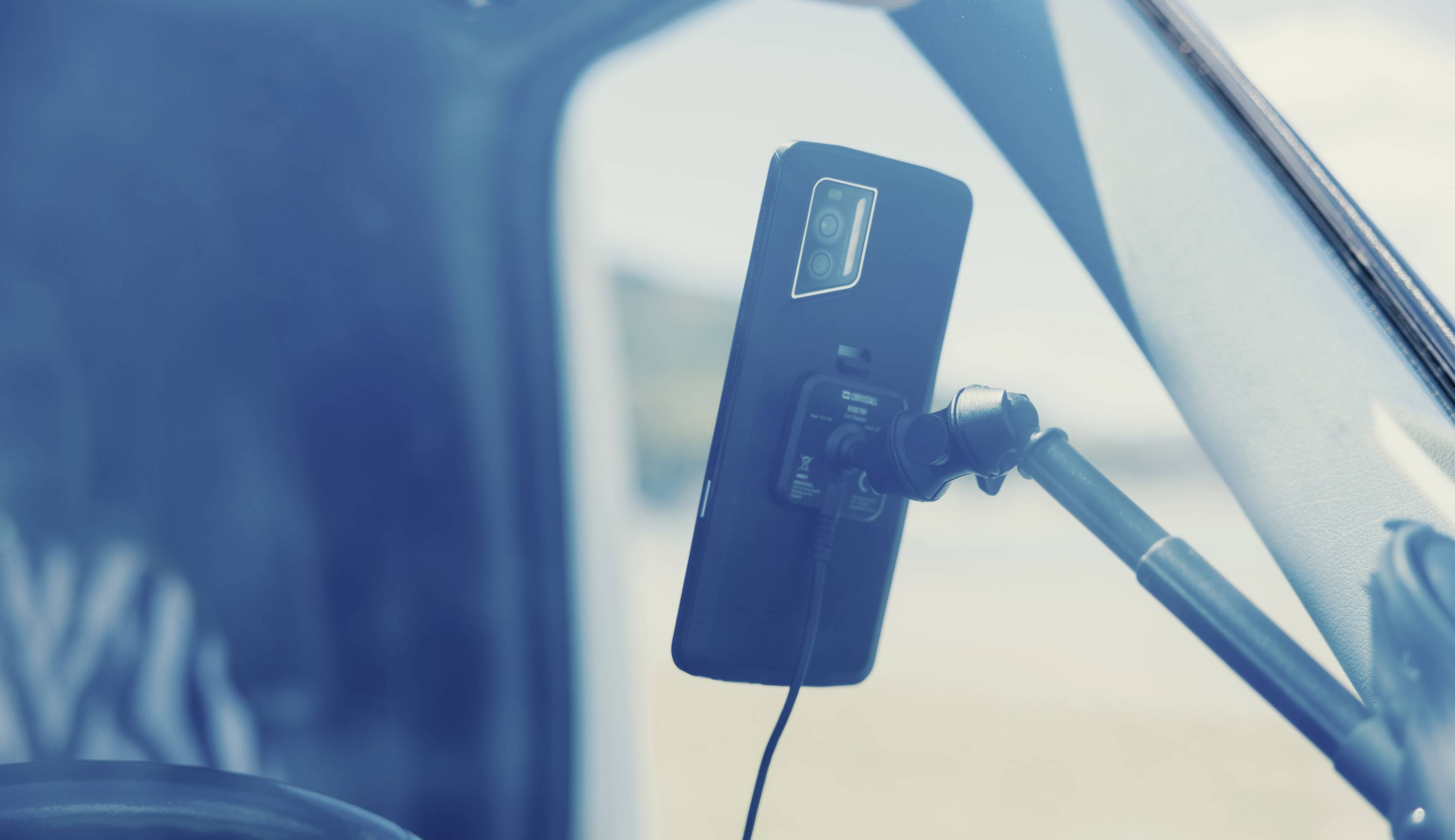 Smartphone mounted on a holder in a car, connected to a charging cable and ready for navigation or hands-free calls while driving.