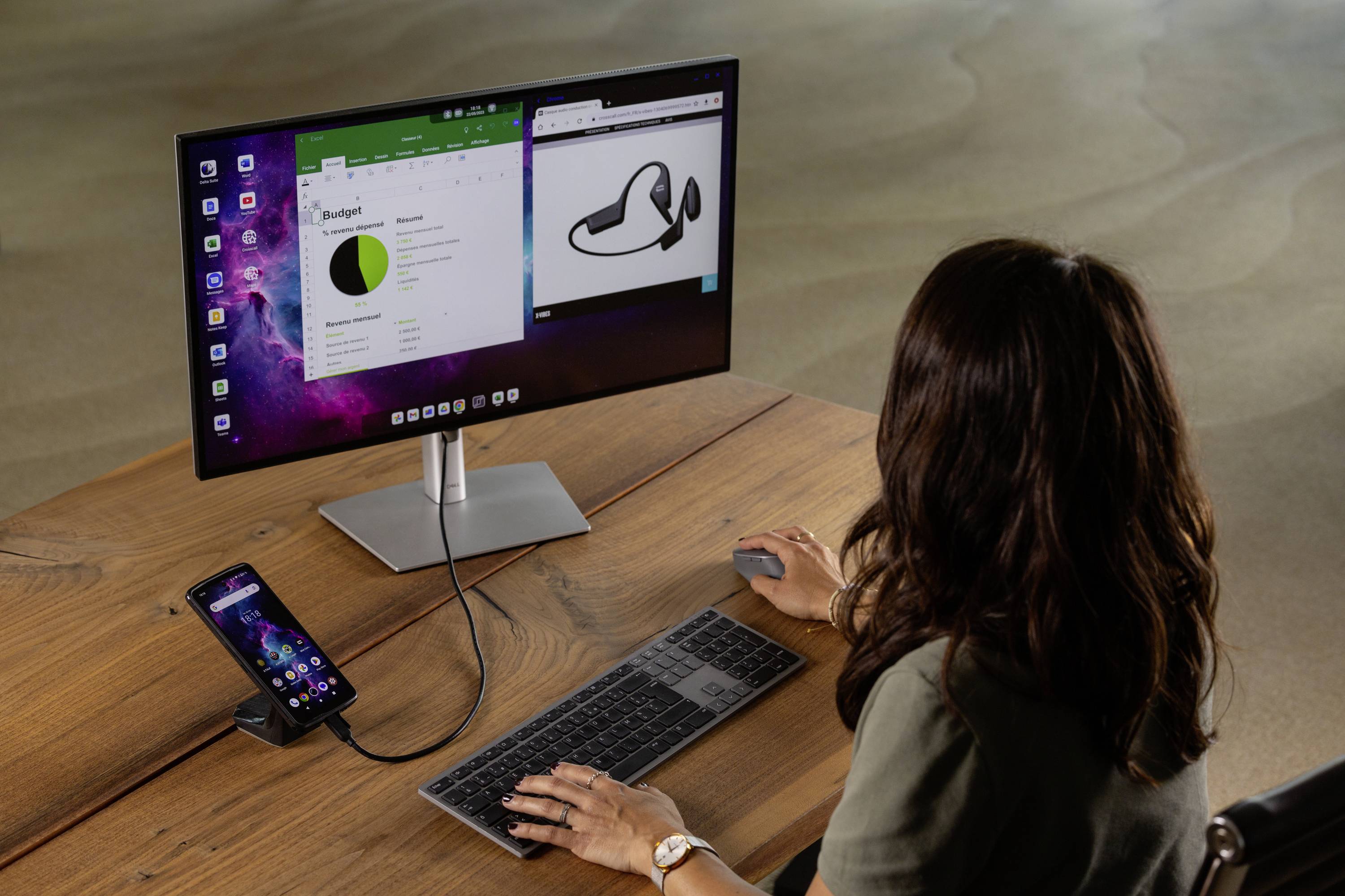 A person is working at a monitor with a keyboard and mouse. A smartphone is connected to the monitor and displays an extended view.