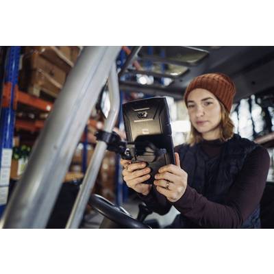 A person wearing a cap is looking at an electronic device in a warehouse with shelves in the background.