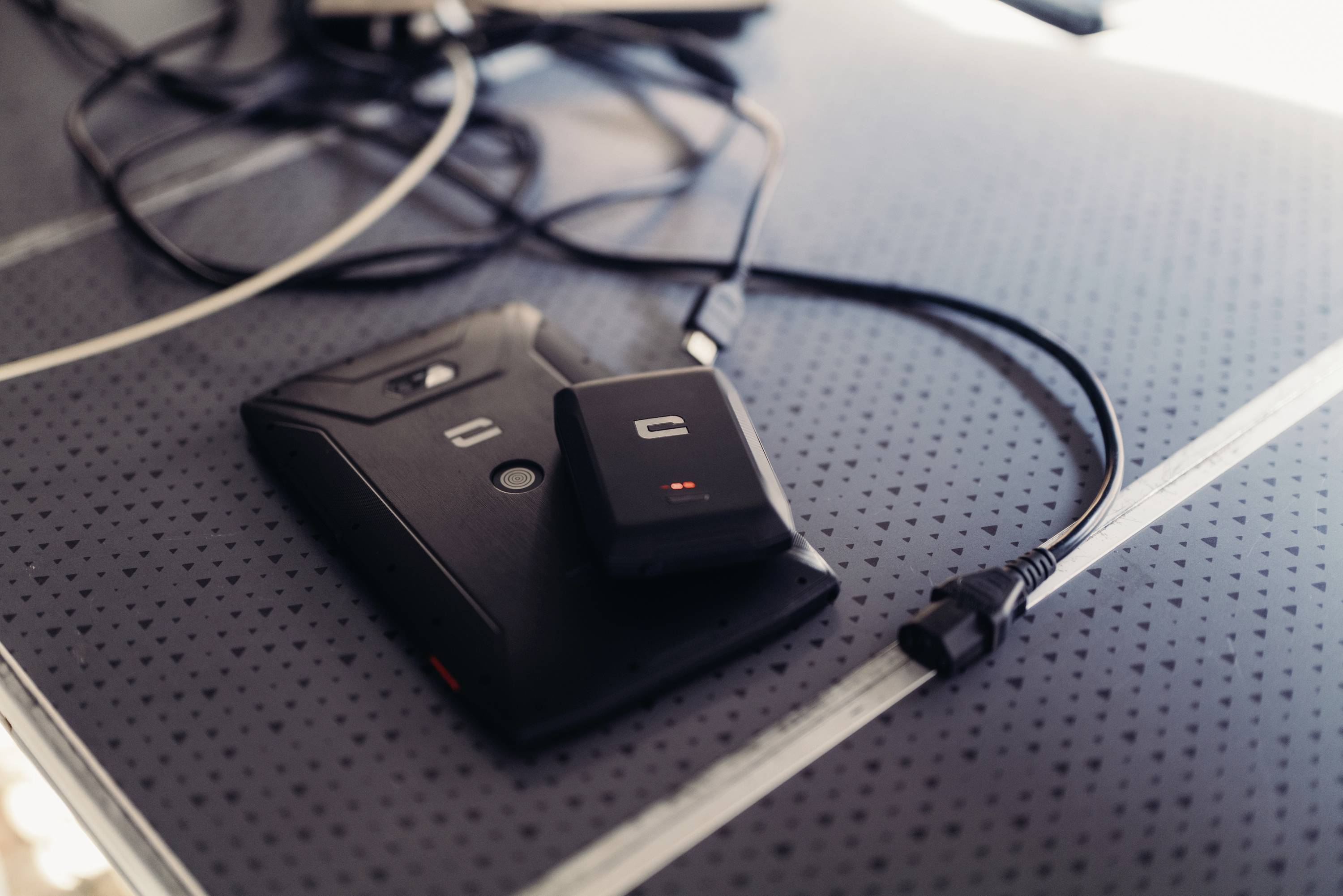 A black wireless charger with a small red light is lying on a table, with a cable connected to it.