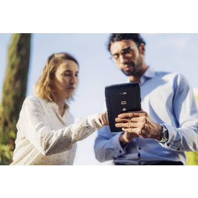 Two people are standing outdoors and looking at a tablet. One person is pointing at the screen. They appear focused and engaged.
