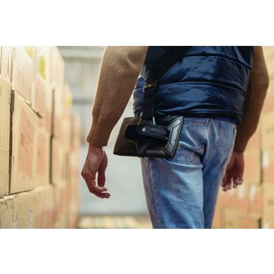 A person wearing a jacket is carrying an electronic device on their hip in a warehouse full of cardboard boxes.