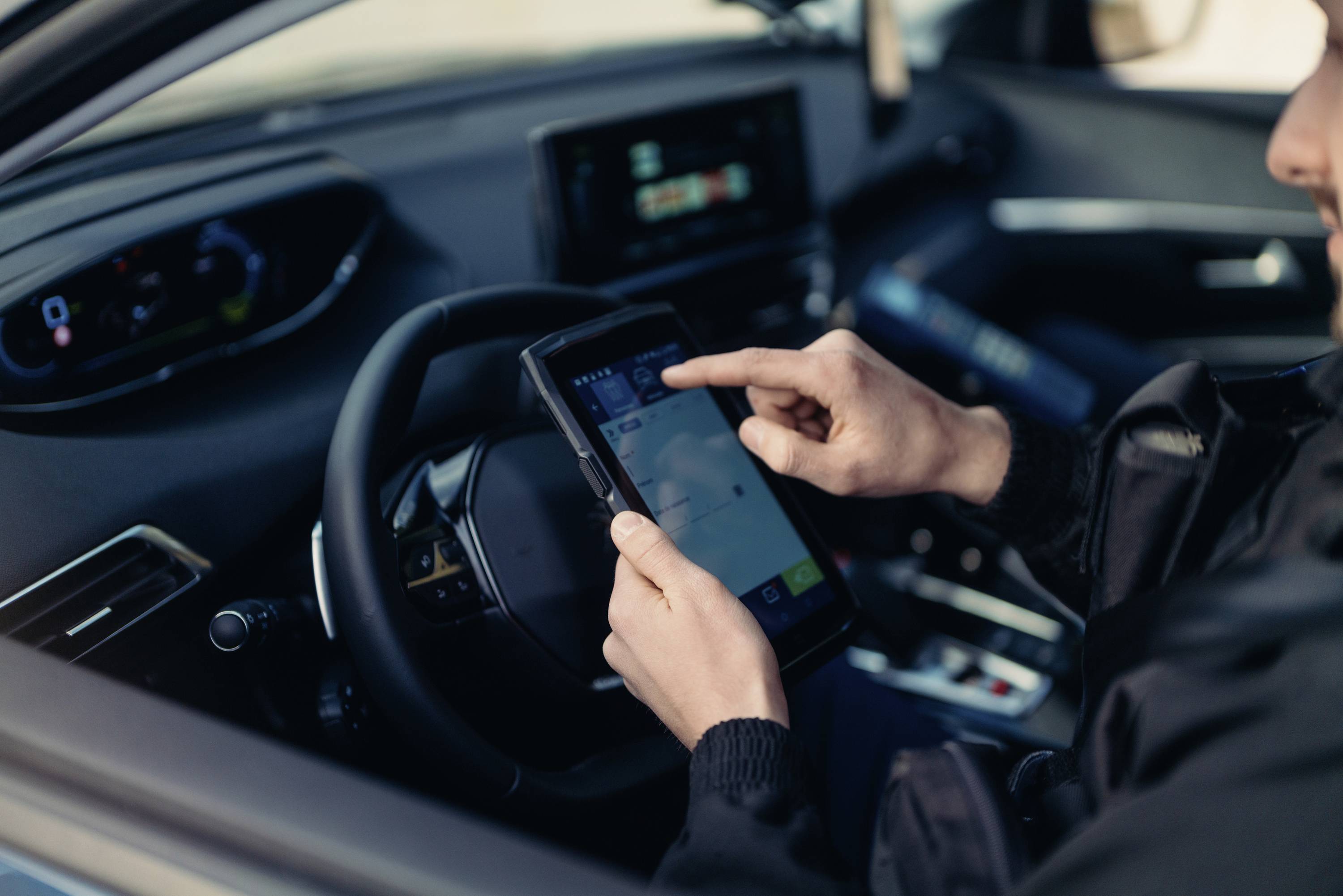 A person is using a tablet for navigation in a car. The screen displays a map view, with the steering wheel and car interior in the foreground.