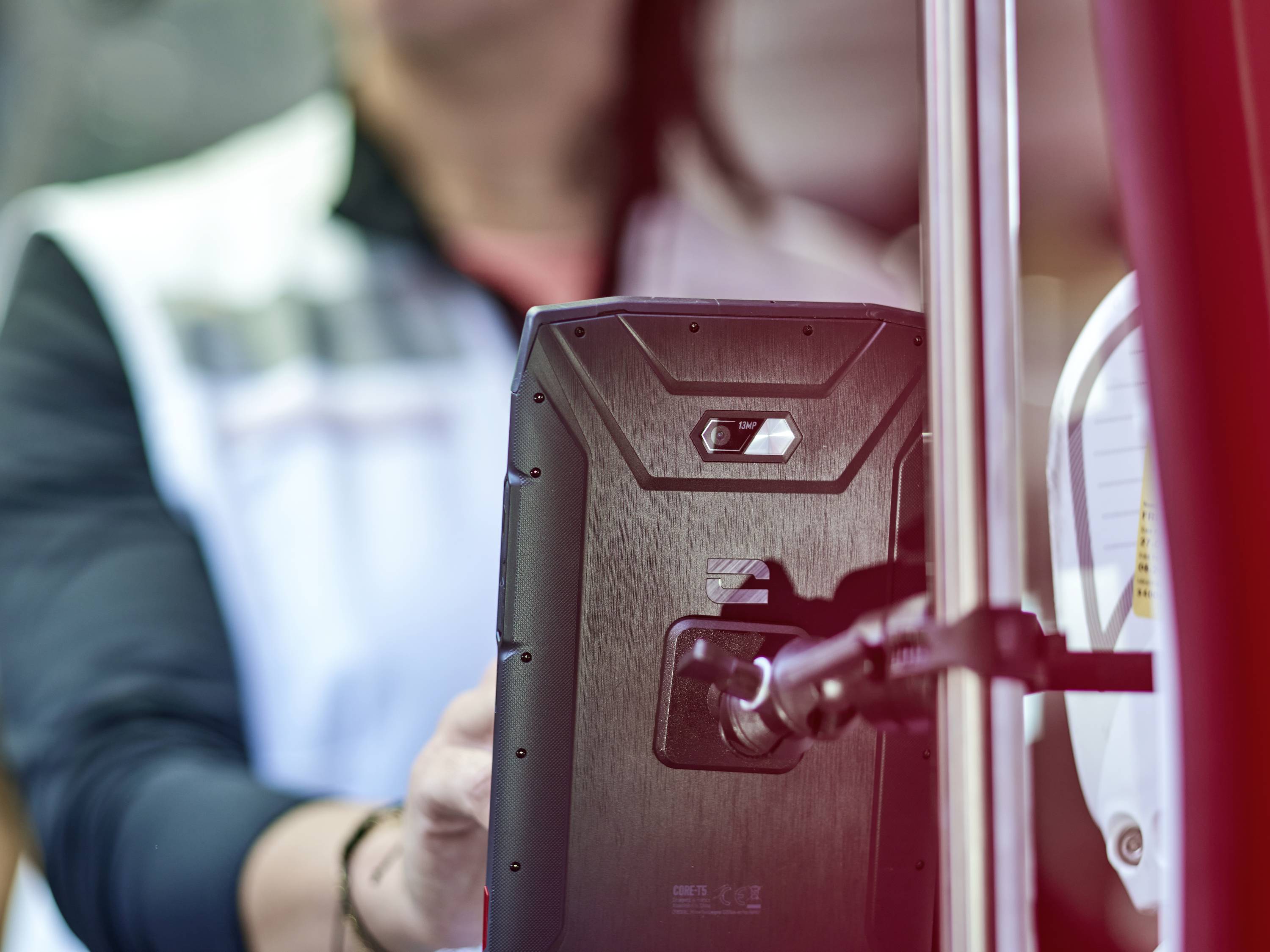 A person is operating a device with a screen at a stand, with a blurred background, focusing on the interaction with the technology.