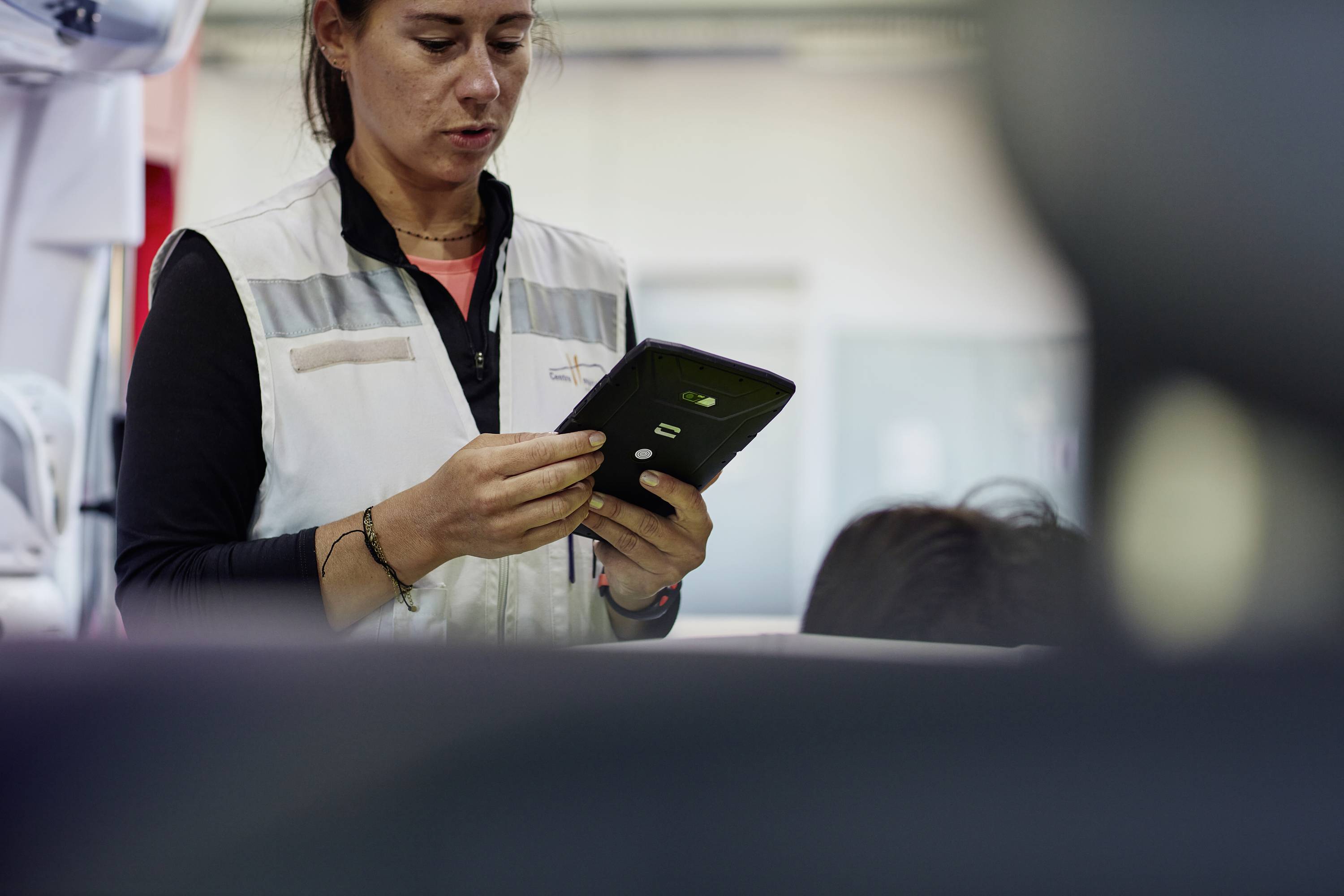 A person in workwear is examining a tablet in an industrial setting.