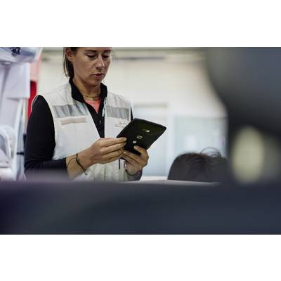 A person in workwear is examining a tablet in an industrial setting.