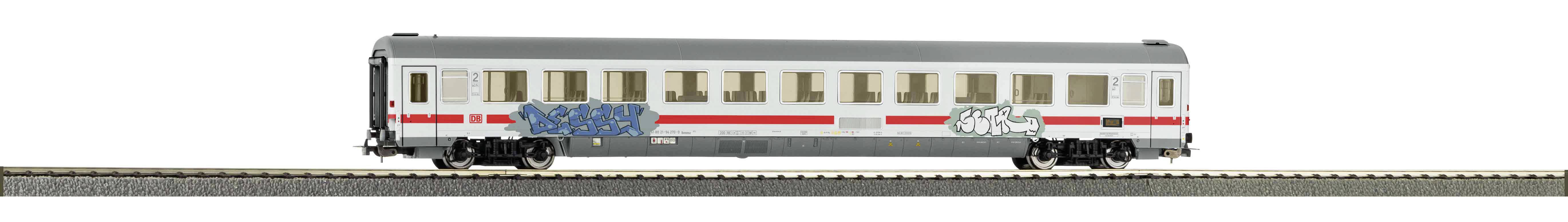 A white train carriage with red stripes and graffiti. The carriage is standing on railway tracks and has several windows.