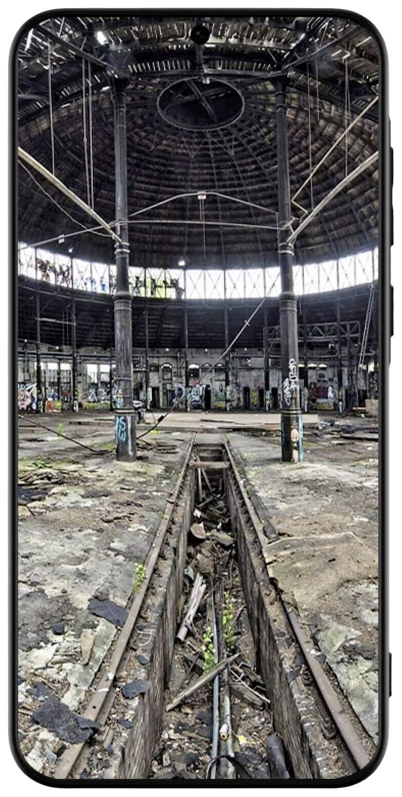 Old, abandoned and dilapidated railway depot with a rounded roof and visible graffiti. Railway tracks run through the building.