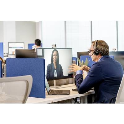 A man wearing a headset is conducting a video call on a computer screen in a modern office. A woman is visible on the screen.