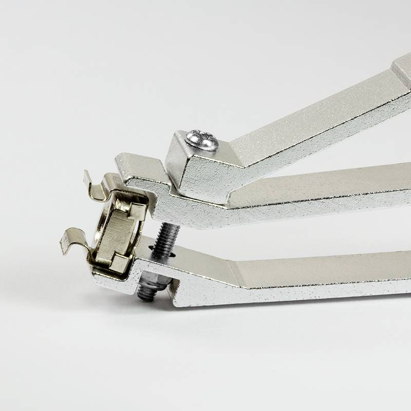 A silver metal tin opener in an open position, placed on a white surface.