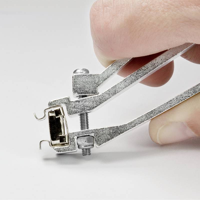 A hand is holding an enlarged metal nail clipper. The clipper shows a closed cutting edge and a shiny, silver surface.