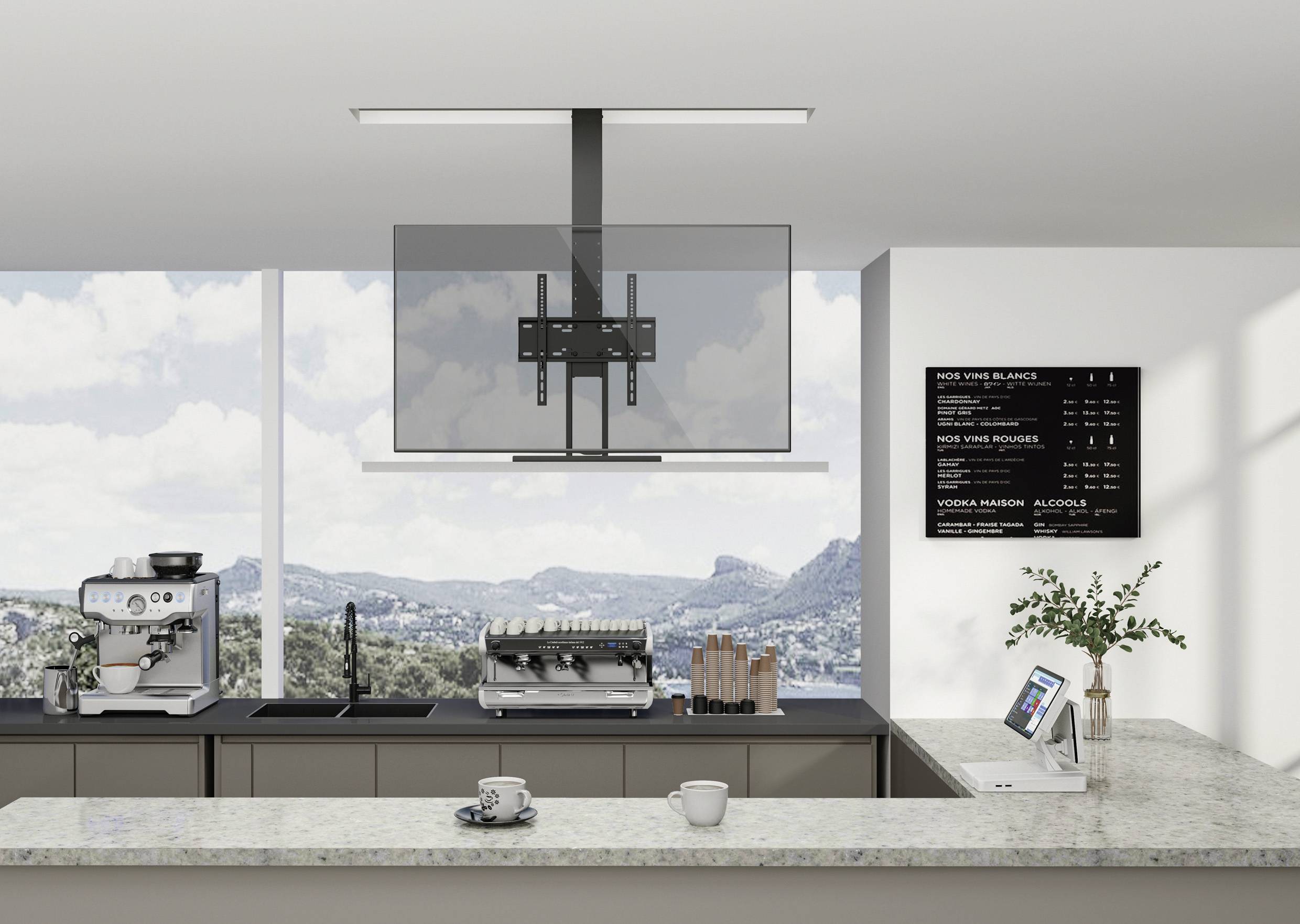 Modern kitchen with a coffee machine, laptop on the counter and a view of mountains through large windows. A menu board hangs on the wall.
