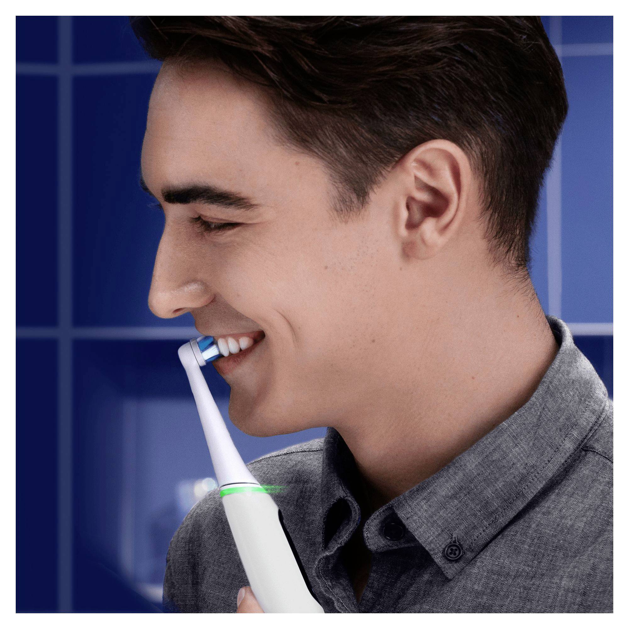 A person is smiling and using an electric toothbrush against a blue background.