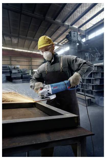 A worker in protective gear uses an angle grinder, creating sparks in an industrial workshop setting.
