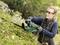 A person is cutting a hedge with an electric hedge trimmer. They are wearing safety glasses and gloves to work safely.