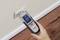 A person is measuring the moisture of a wall using a digital moisture metre. The device displays '0.0 %' on the screen.