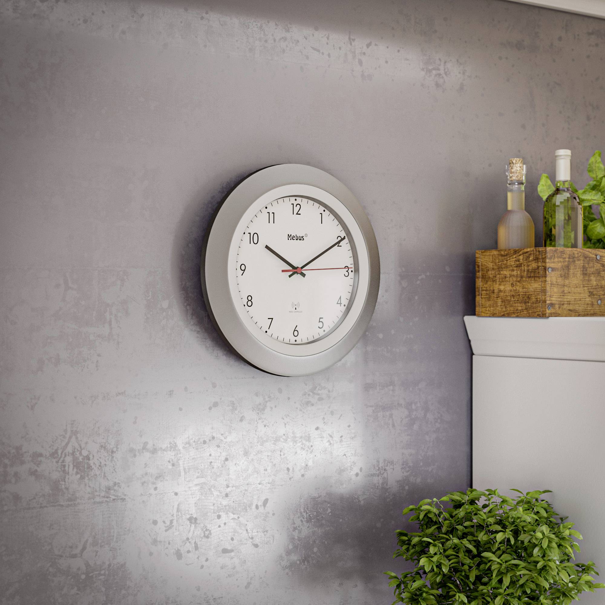 On a grey wall hangs a round clock with a white dial and black hands. Next to it, bottles are placed on a wooden shelf.