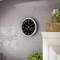 A round wall clock with a black dial and white numbers shows the time as 10:09. A plant is visible in the bottom left.