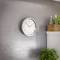 A wall clock shows 10:10. Next to it, on a shelf, is a wooden box with green plants, including a round vase.