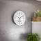 Wall clock shows 2:54; next to it a shelf with plants and bottles; modern, minimalist interior design.