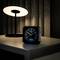 A clock on a table next to a lamp. The clock shows 7:00 and 23°C. The lamp's light is warm and soft.