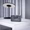 A digital alarm clock shows '13:08' and 'Saturday, 5th October'. In the background, a modern, black lamp stands on a white table.
