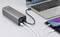 A grey power bank is charging a laptop and a smartphone simultaneously. Various cables are connected.