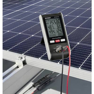 Digital measuring device displays values from solar panel. Measuring device connected to tilted solar panel with cables. Readings visible.