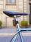 Bicycle seat of a blue bicycle, which is parked on a cobblestone street in front of a historic façade with round plant pots.