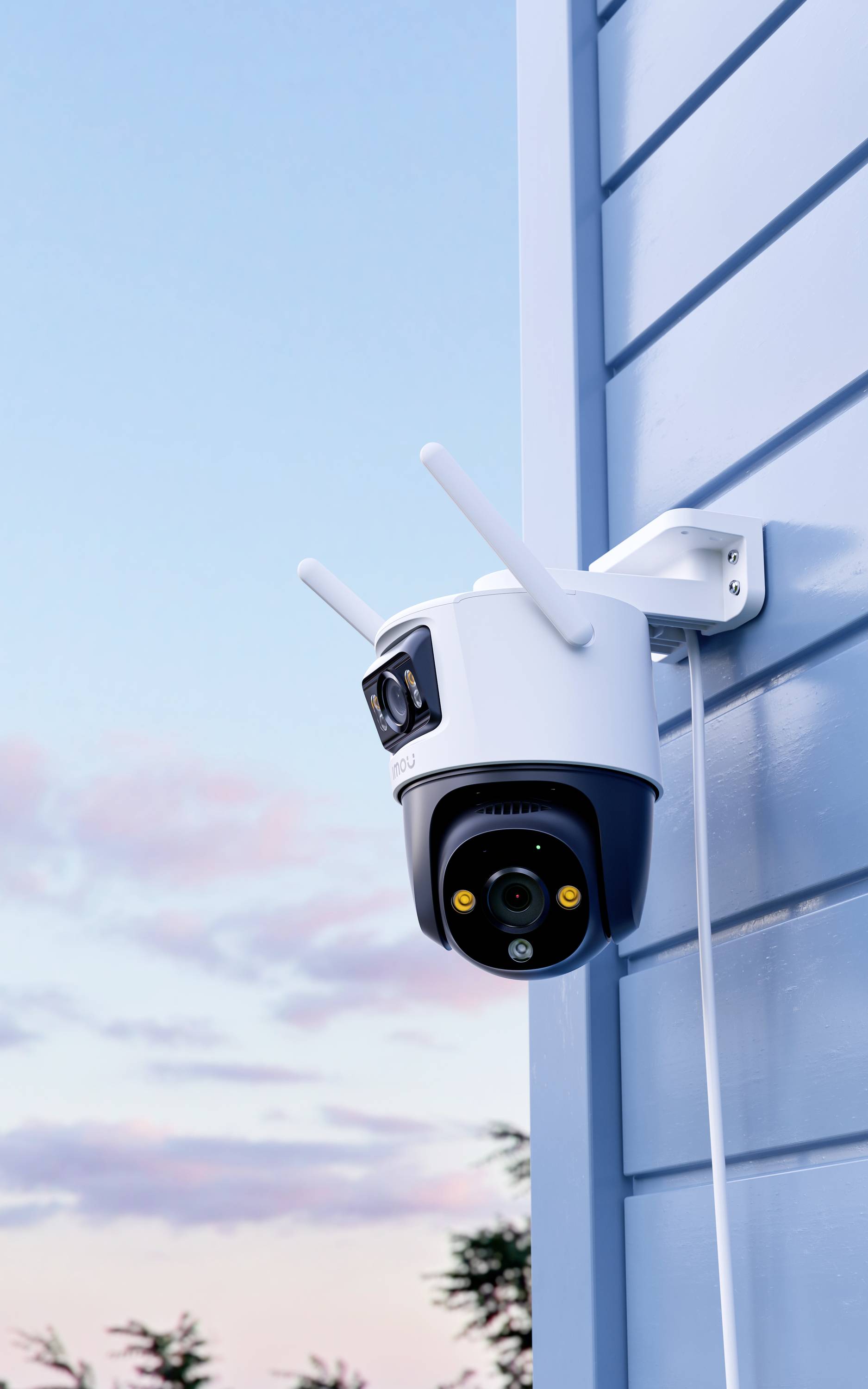 A surveillance camera with aerials is mounted on the blue external wall of a building, with a view of a cloudy sky in the background.