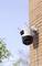 Surveillance camera mounted on a brick wall, facing outwards with a clear sky and scattered foliage in the background.
