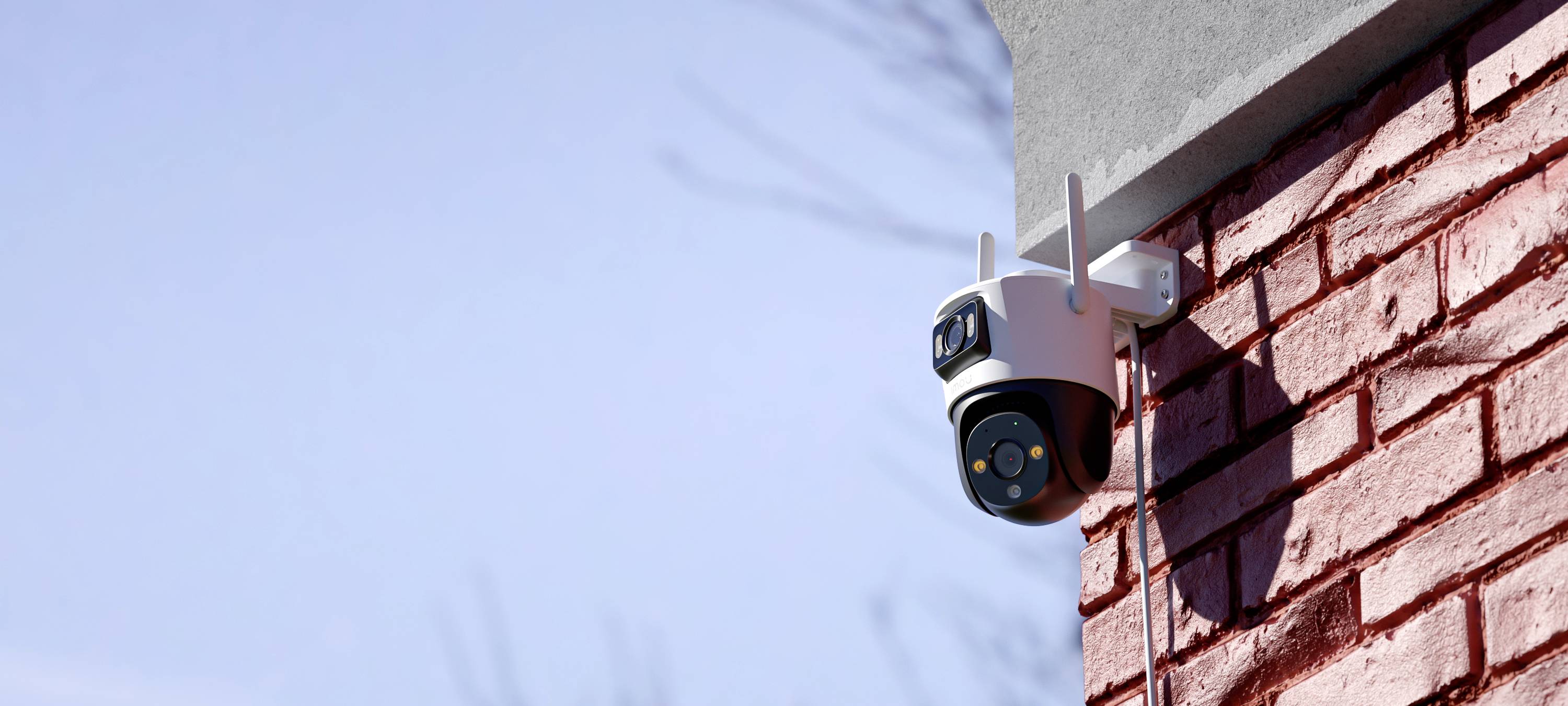 A security camera mounted on a red brick wall, facing right; blue sky in the background.