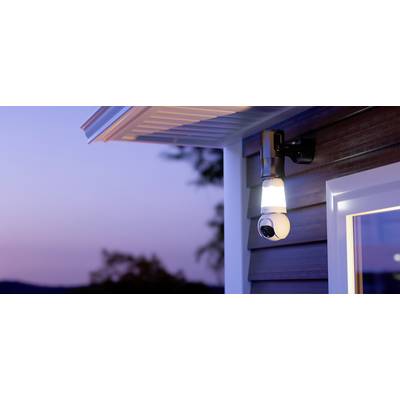 External camera with integrated lighting mounted on the house wall, illuminating in the evening light, monitoring the entrance area.