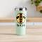 A mint-coloured mug with a stylised bee logo and the text 'Be Kind' sits on a table. Blurred kitchen elements are visible in the background.