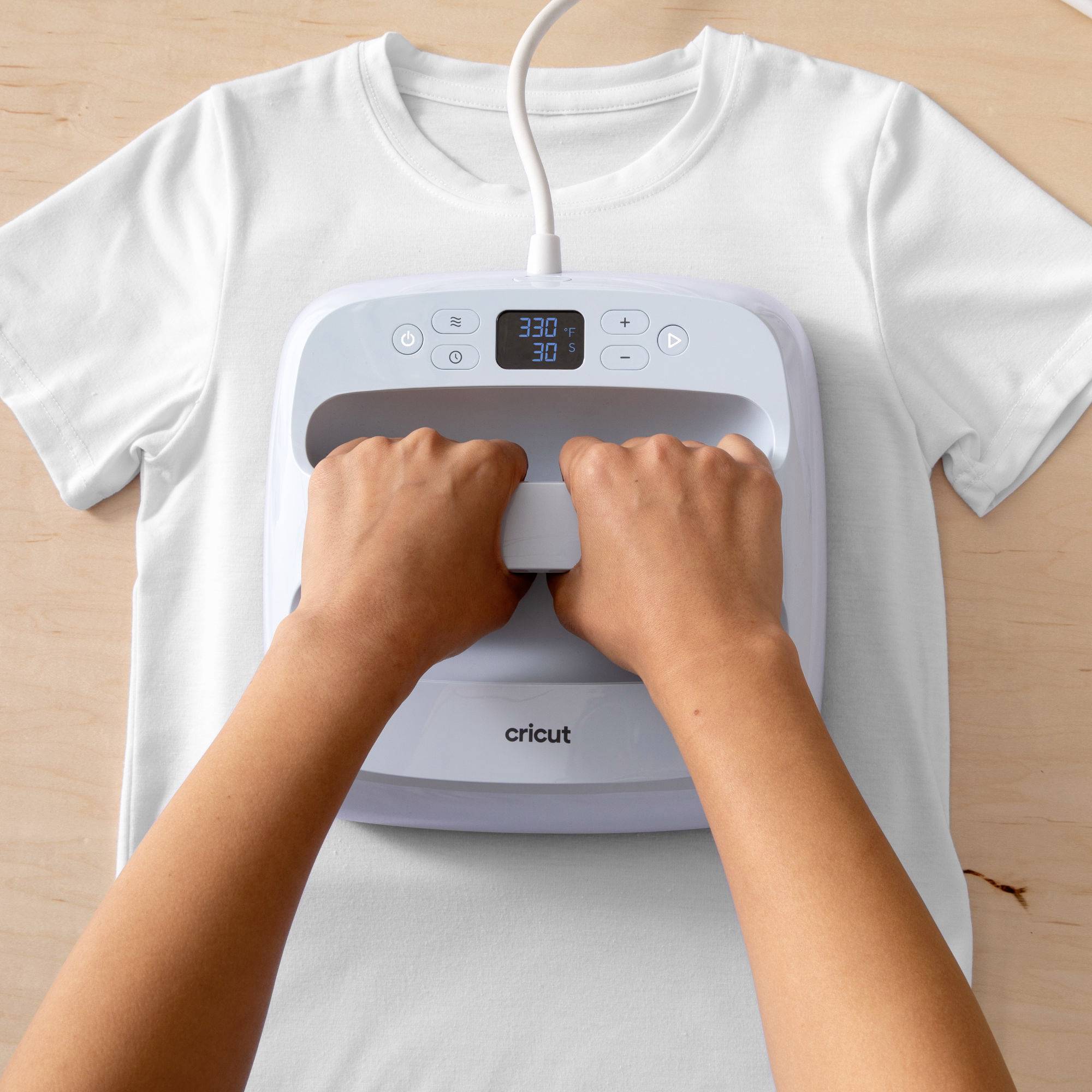 A person is ironing a white T-shirt with an iron displaying a digital temperature of 330 degrees Fahrenheit and a timer of 30 seconds.