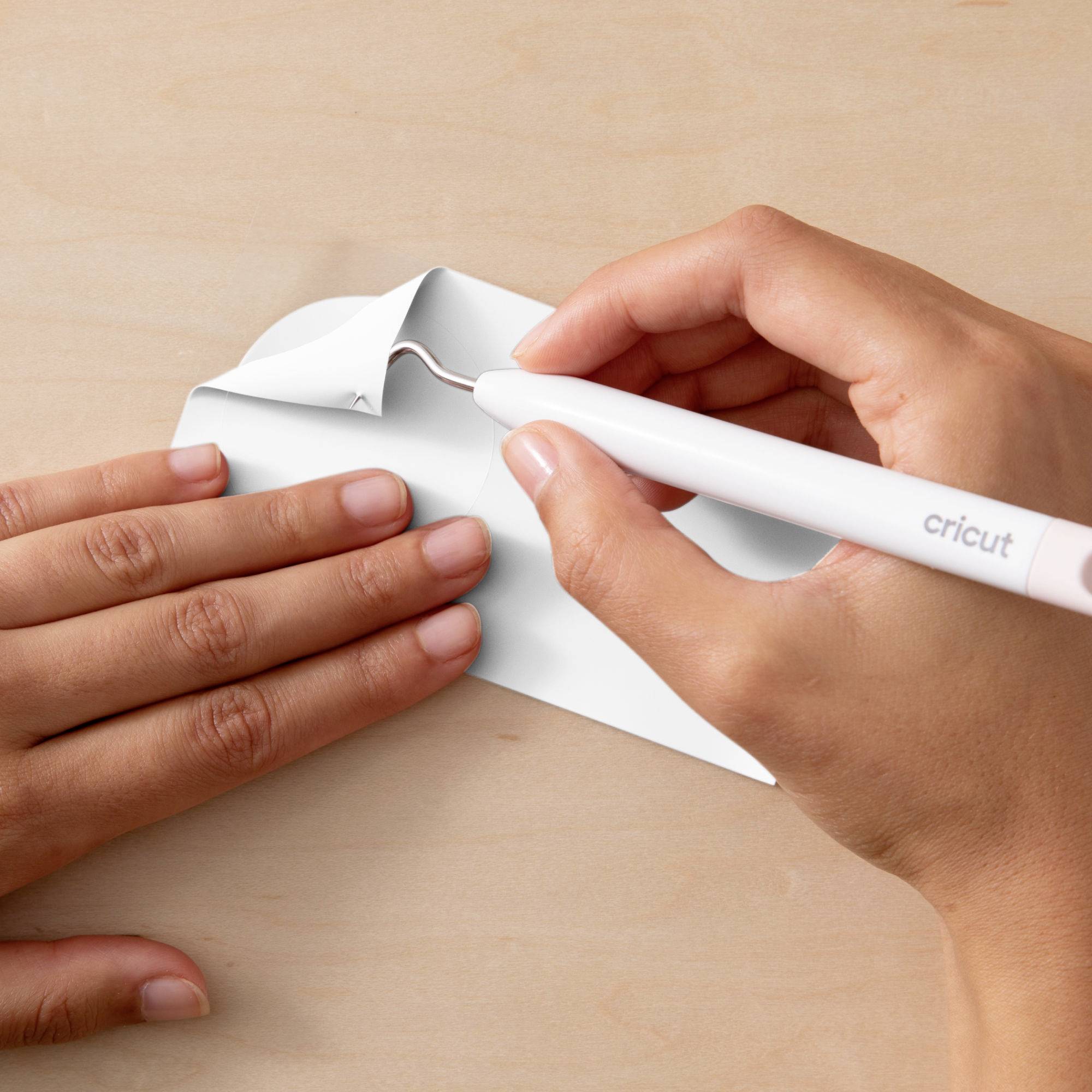 Two hands are working with a Cricut tool to cut paper precisely.