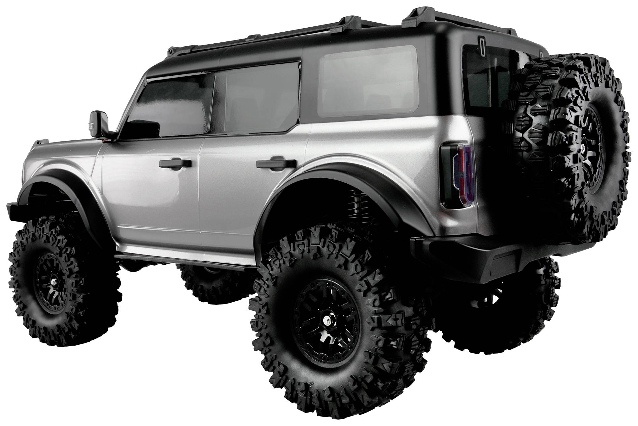 Silver off-road vehicle with large off-road tyres, viewed from the rear side angle. The vehicle has a robust design and a spare wheel at the rear.