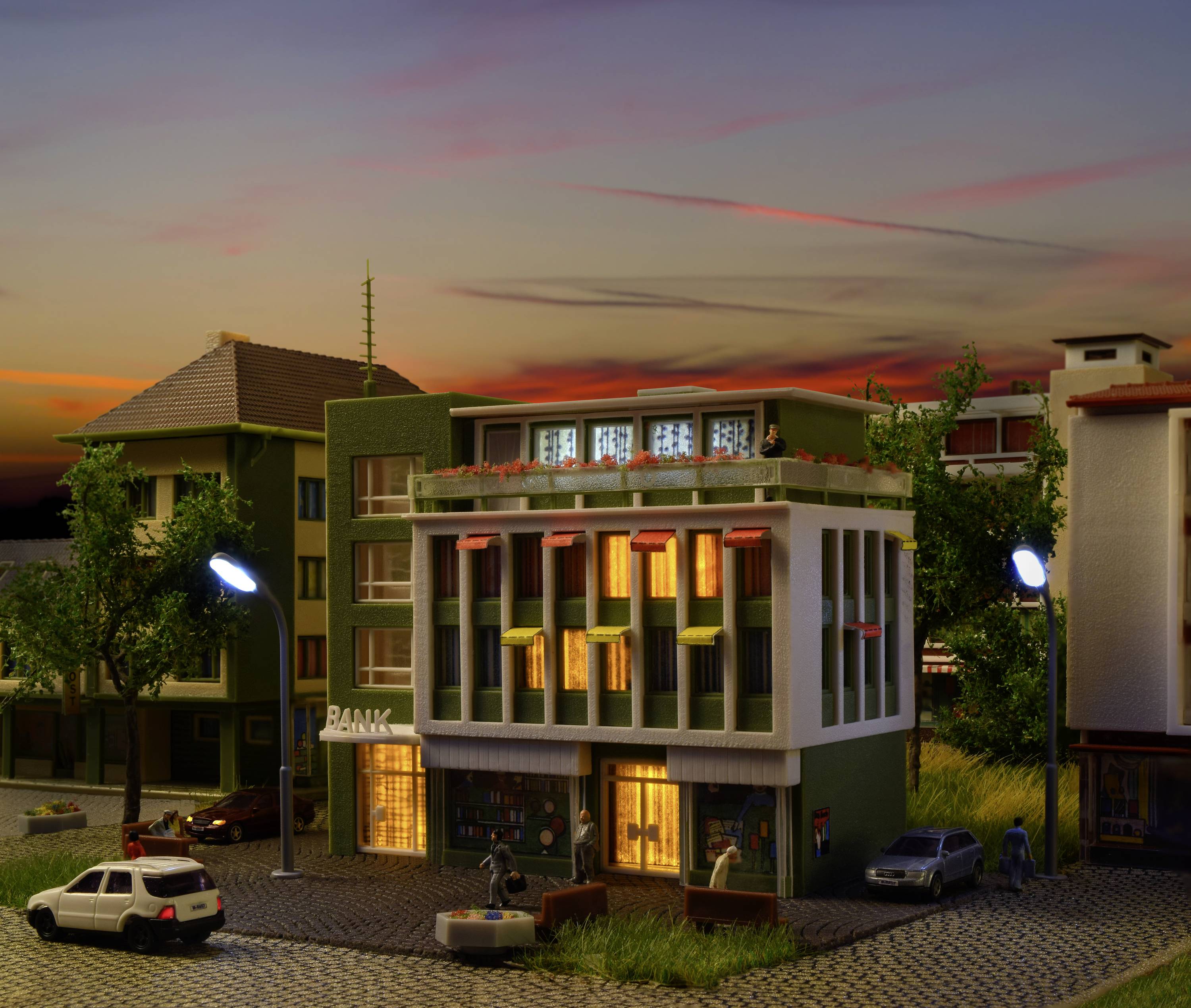 A modern townhouse at sunset with illuminated windows, with a small car and people in front of it.